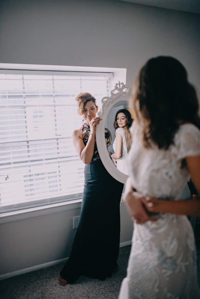 bride looking at herself and the back of her wedding dress in the mirror, held by one of the members of the wedding party, Orlando, FL