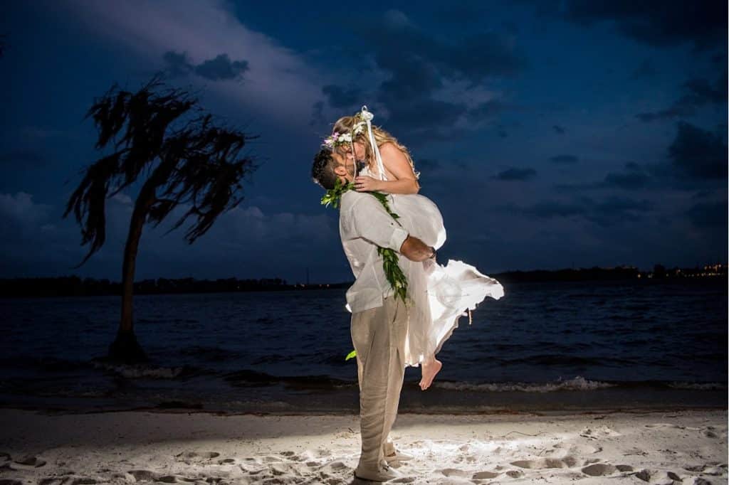 groom lifting his bride up on the beach, at night, blue sky, paradise cove, central fl