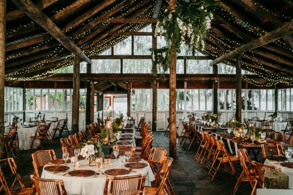 tables and chairs set for a wedding reception, large windows, wood rafters, wood chairs, white tablescloths, gold chargers, central fl