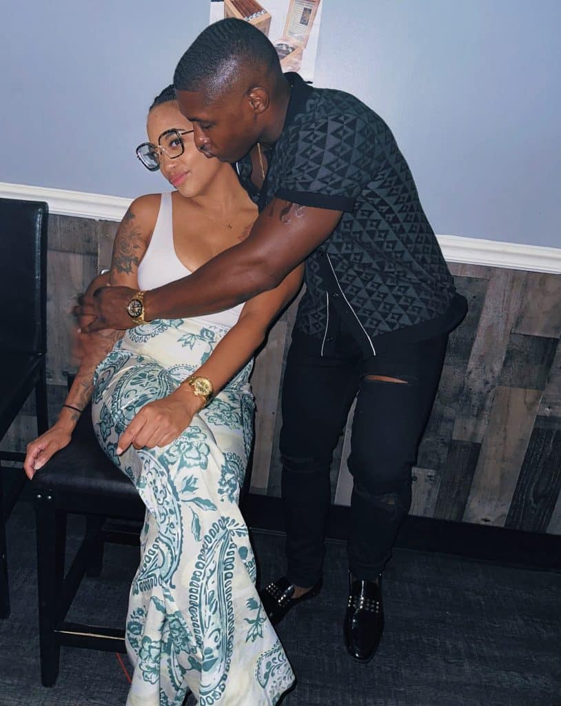 woman sits in chair wearing long skirt while man stands next to her hugging