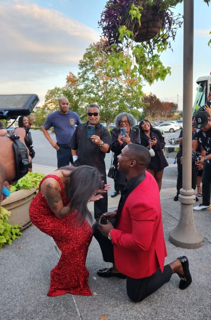 man kneels in front of woman bent over in surprise proposing marriage