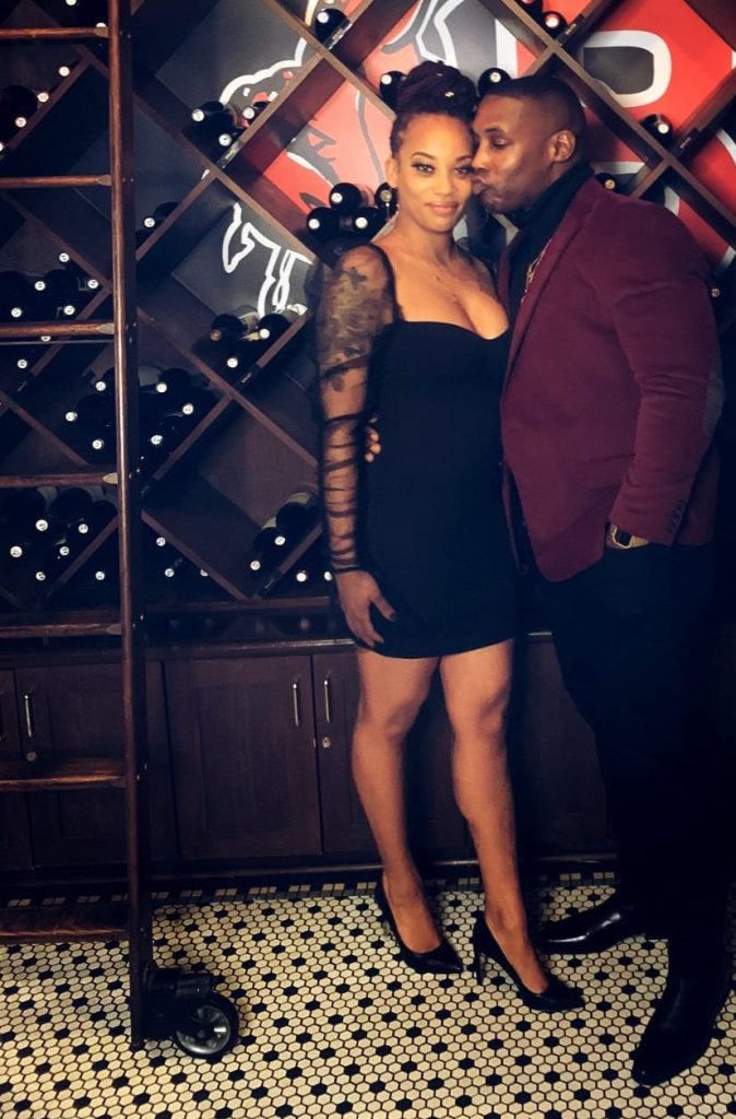 couple pose for picture in front of wine rack