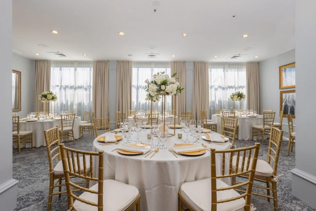 room set up with white tablecloths, gold chargers, gold chairs with white cushions, tall centerpieces with white flowers, Castle Hotel, Central FL
