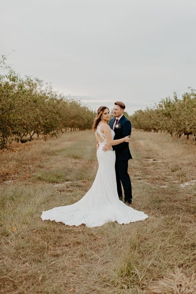 Bride and groom posing in a field of orange trees