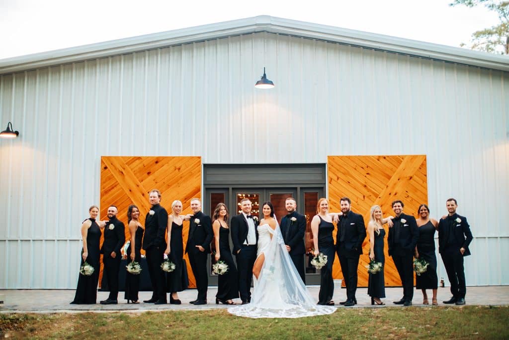Large facility with wooden doors and the bridal party all in black posing for the camera