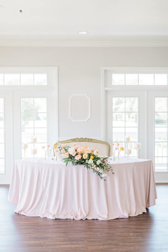head table set up with a light pink tablecloth on an crescent shaped table, floral arrangement on the front, couples sofa for the bride and groom, Orlando, FL