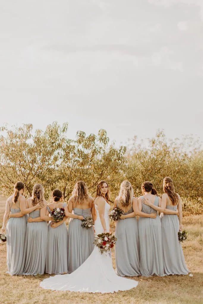 Bride with her bridesmaids. The bridesmaids are facing away in stormy grey dresses and the bride is in the middle looking at the camera