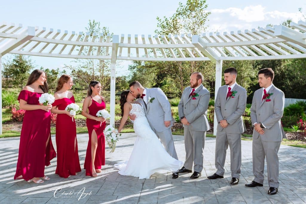 groom dipping his bride while kissing her, with wedding attendants other both sides, white pergola behind, Orlando, FL