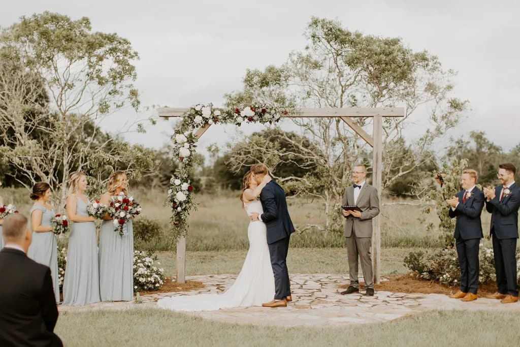 Bride and groom kissing near their wooden arch after exchanging vows