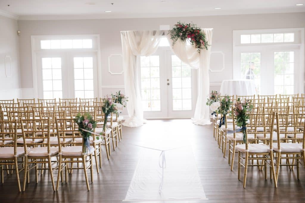 ceremony set up with rows of chairs, center aisle, white carpet down the middle, square pergola with white fabric and greenery on the top right corner, Orlando, FL