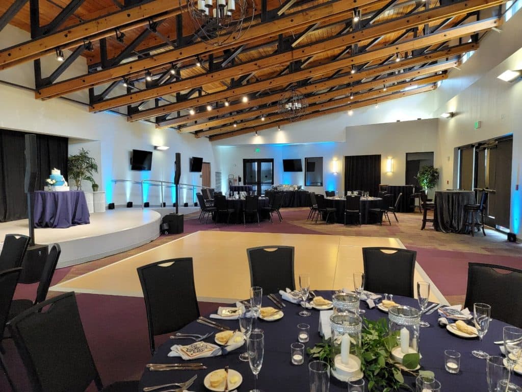 indoor view of the cultural center, black tablecloths, black chairs, votive candles in the center of the tables, wooden beam rafters, stage with a dance floor in the center, Orlando, FL