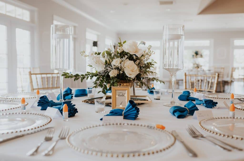 close up of a table set for a reception, round table, white tablecloths, blue napkins, white flower centerpieces, clear chargers, Orlando, FL