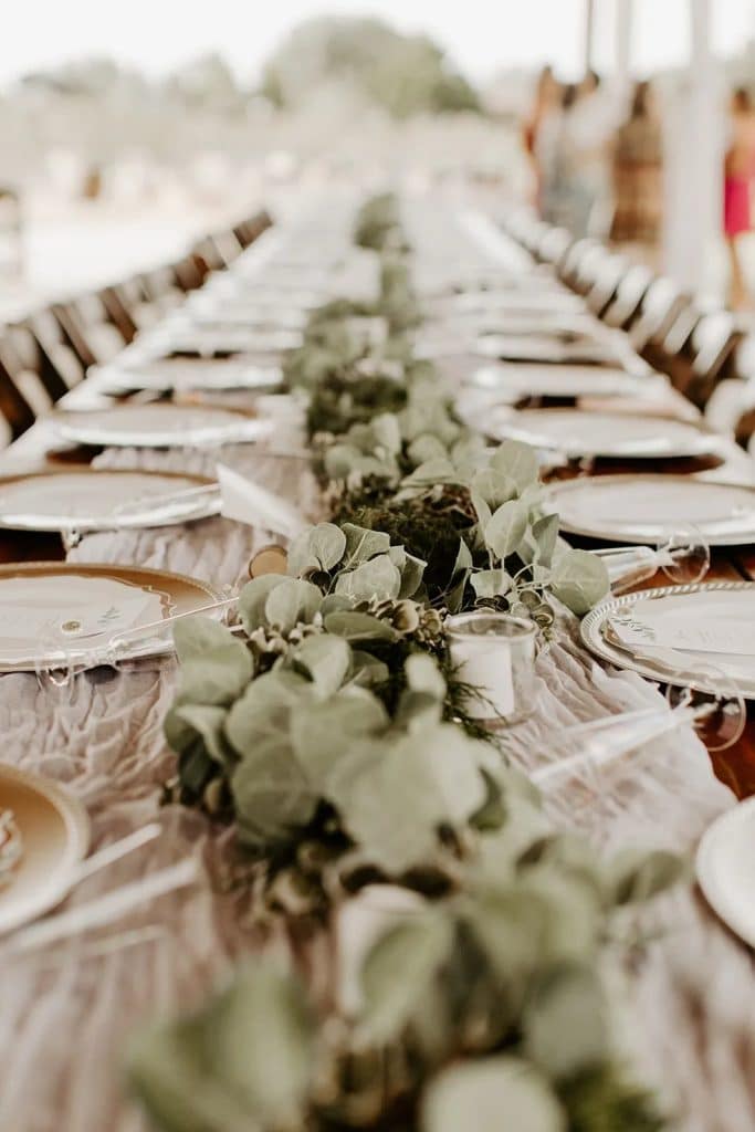 tablescape for a reception, white and green flowers down the middle, white plates with gold chargers