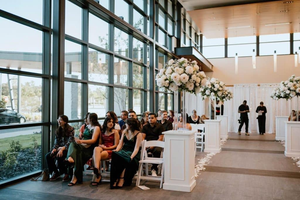 guests waiting for the wedding ceremony to start, large windows, white columns at the end of each row of chairs, tall flower displays, Orlando, FL