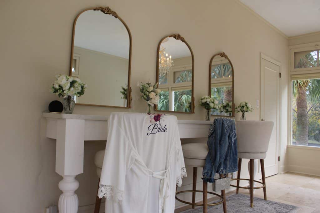 bridal suite at the venue, bride's robe handing on the chair, 3 mirrors on the wall, white flower vases on the mantle, The Mulberry Estate, Orlando, FL