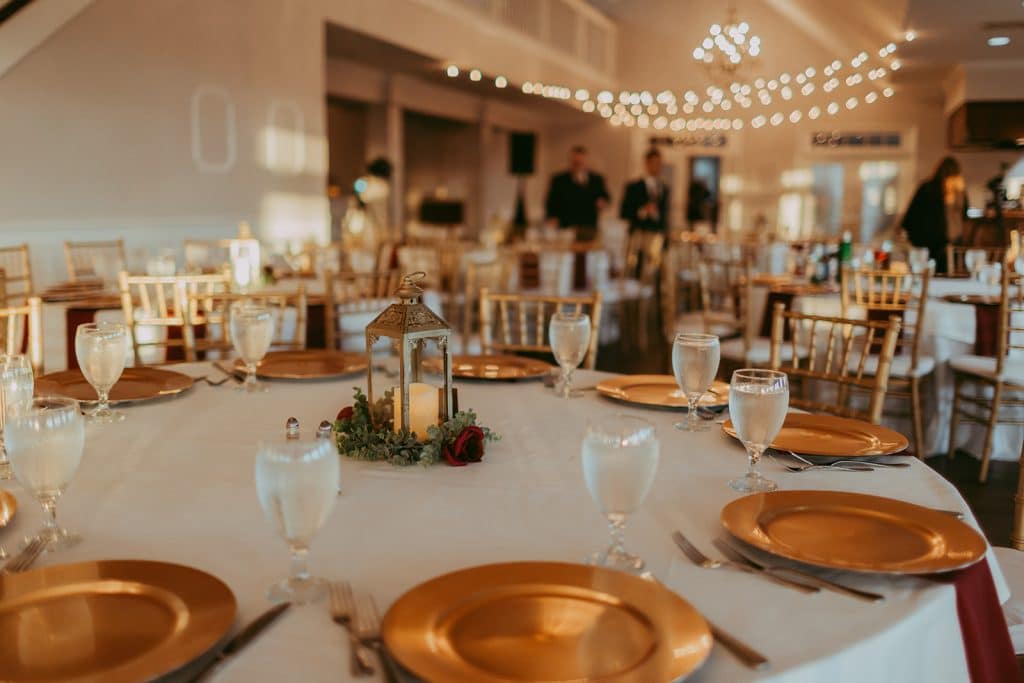 reception set with round tables, white tablecloths, gold chargers, red napkins, twinkle lights in the background, Orlando, FL
