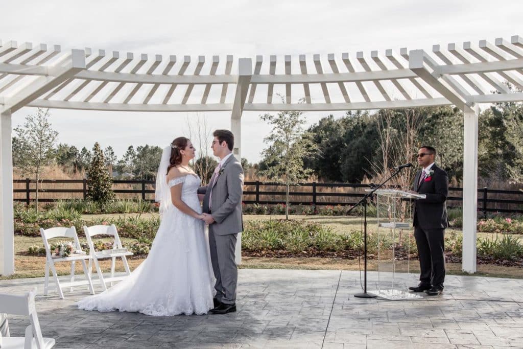 bride and groom holding hands under the pergola, officiant off to the right side with a podium and microphone, outdoors, The Center at Deltona, Orlando, FL
