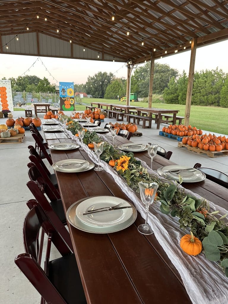 pavilion set up for a reception with pumpkins and greenery down the middle, long wood tables, white plates and gold chargers, Acres of Grace Family Farms, Orlando, FL
