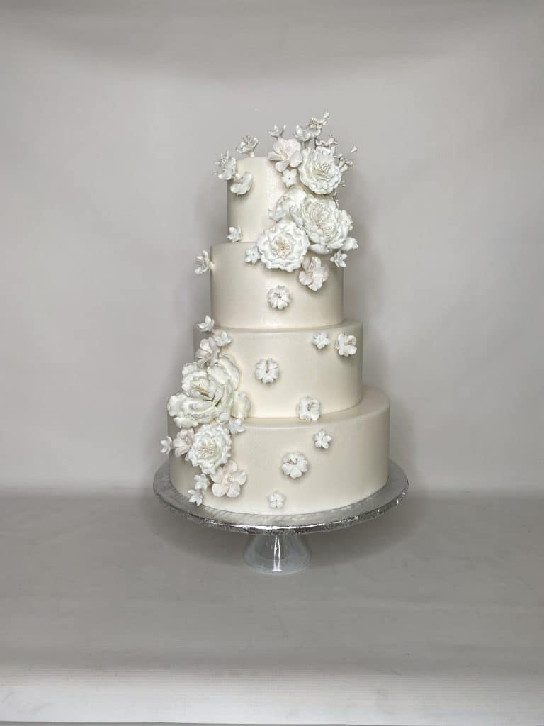 Four tiered white wedding cake, white flowers adorning all sides, clear cake stand, Sugar Divas Cakery, Orlando, FL