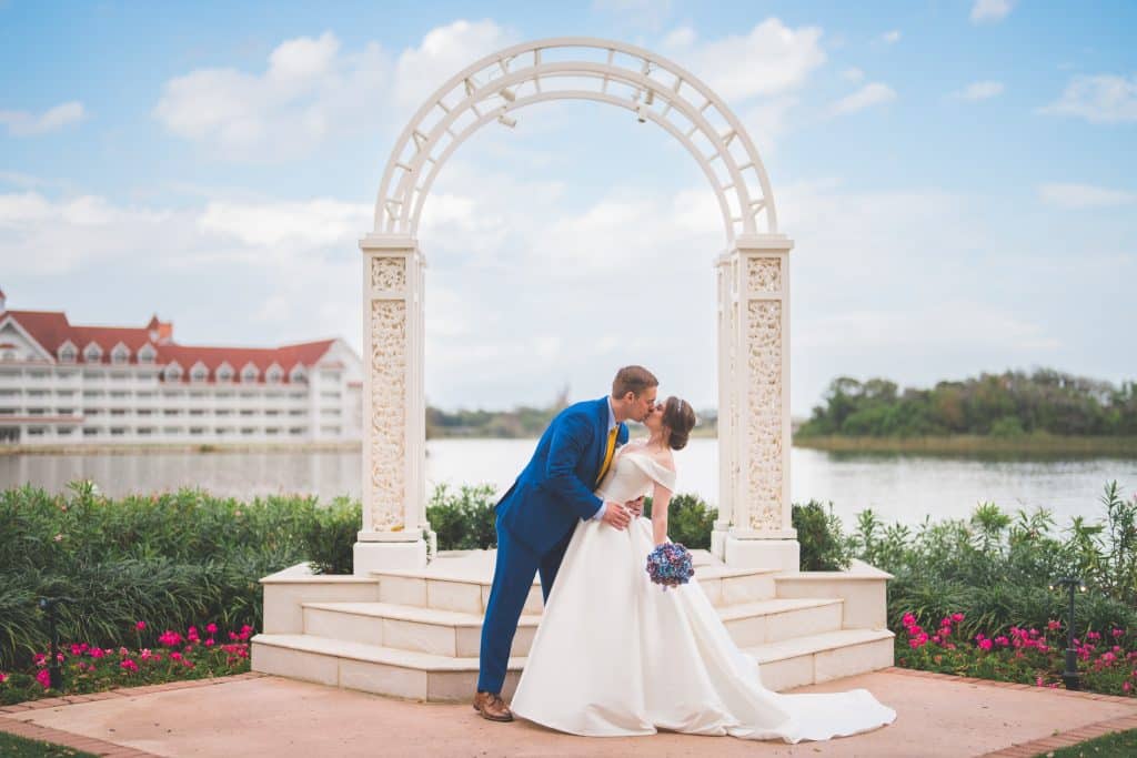Bride and groom kissing under a white arch, in front of a lake near the Grand Floridian Hotel at Disney World, Central FL, Polk Bros Photo.Video.DJ