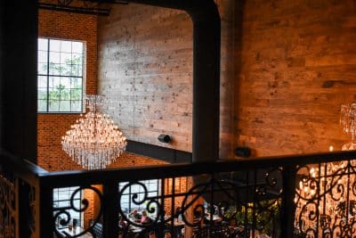 Crystal chandelier and ornate wrought iron railing viewed from upper balcony at New York Beer Project wedding venue in Winter Garden Florida, showcasing the romantic industrial ballroom interior with exposed brick walls and reclaimed wood accents