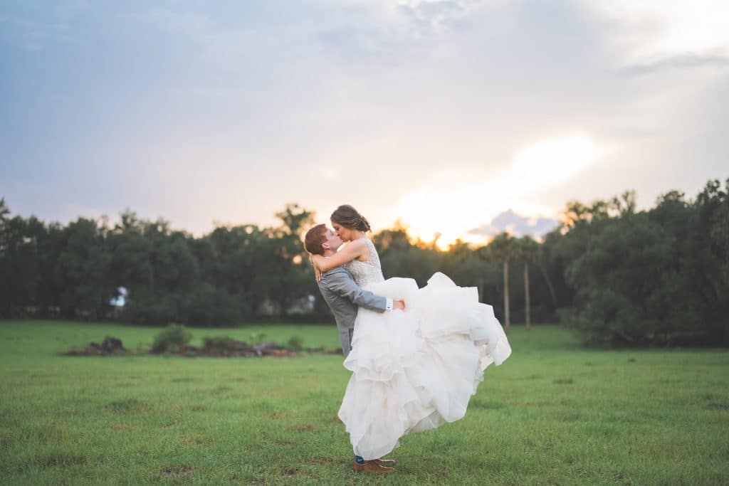 Groom lifting his bride off the ground, outdoors in a field at sunset, Central FL, Polk Bros Photo.Video.DJ