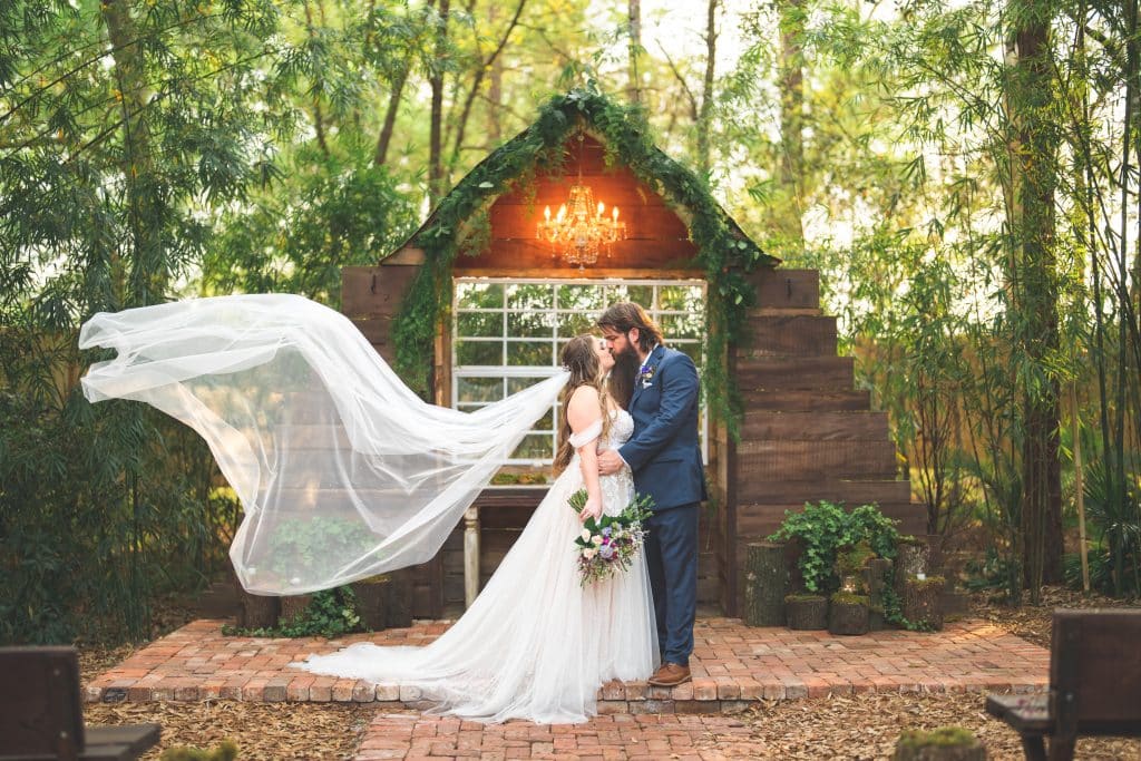 bride and groom kissing, bride's veil blowing in the wind, wooden structure with a window, brick stage, Central FL