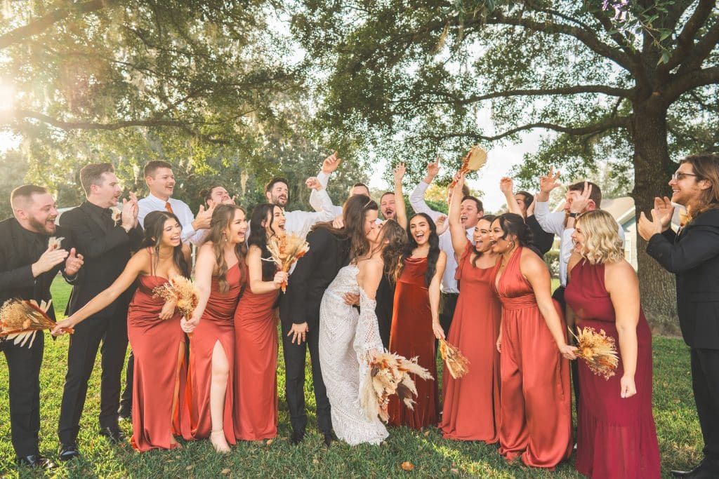 wedding party celebrating, women in shades of red dresses, men in black suits, outdoors, Central Fl