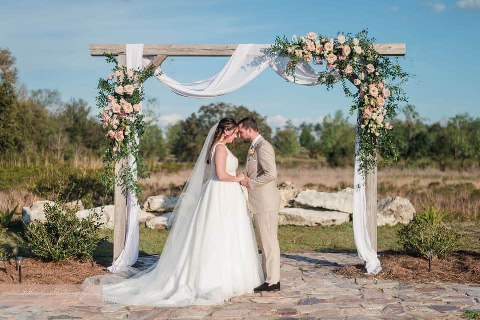 bride and groom at the pergola, adorned with flowers and white fabric, acres of grace family farms, Orlando, FL