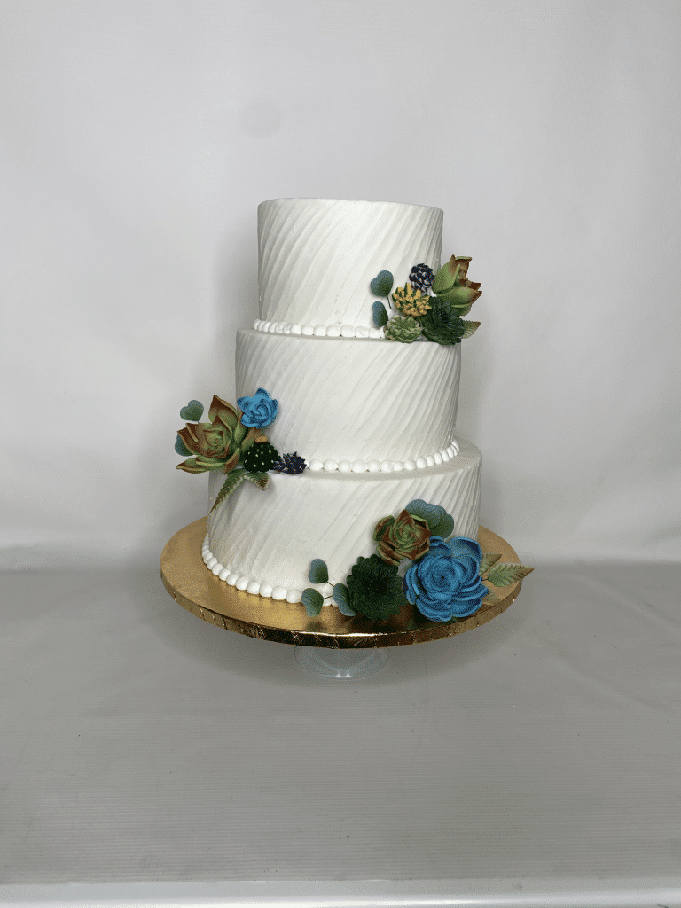 three layer cake, white fondant, pearls around the bottom of each layer, blue flowers with green leaves on the edges of each layer, Orlando, FL