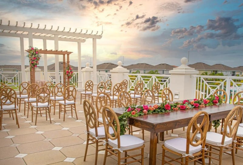 Rooftop patio, altar, wooden chairs set for the ceremony, table with wooden chairs, red flowers and greenery down the middle, Rentyl Resorts, Orlando, FL