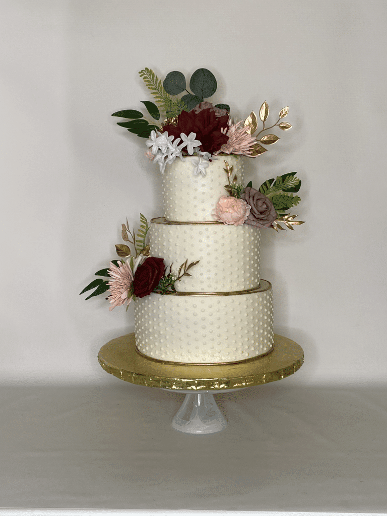 Three layer cake, gold ribbon on the top of each layer, gold cake stand, pink and green flowers with gold leaves, Sugar Divas Cakery, Orlando, FL