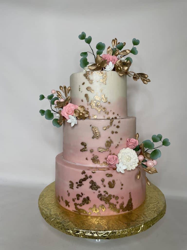 three layer cake with shades of white and pink layers, gold embellishments, with pink and white flowers, green leaves, gold foil covered cake plate, sugar divas cakery, orlando, FL