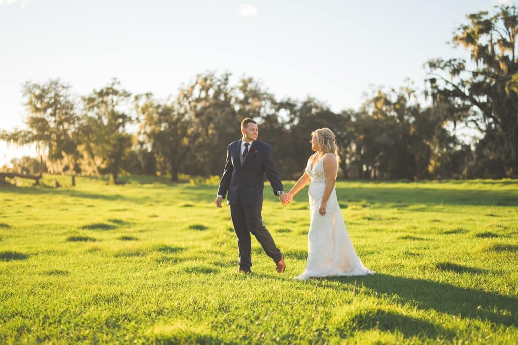 groom leading his bride hand in hand, walking in a field, Central FL, Polk Bros Photo.Video.DJ