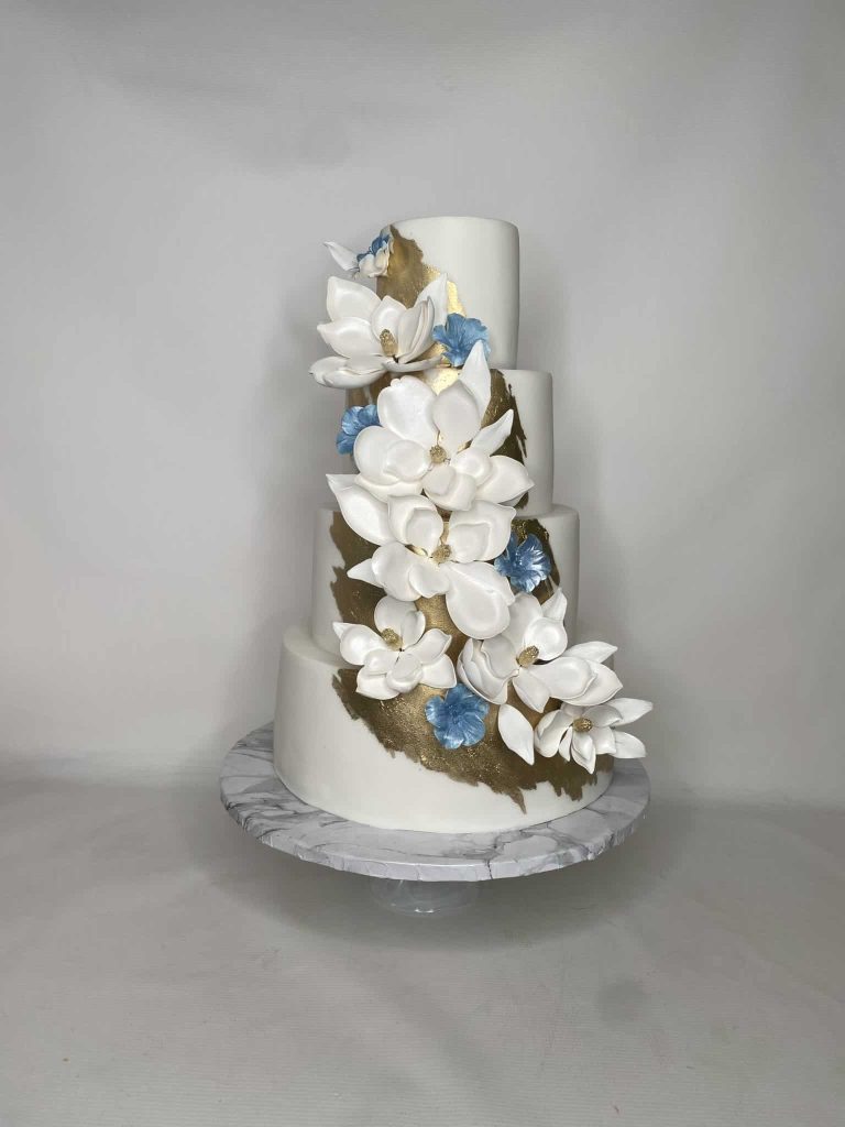 four tiered wedding cake, all white flowers, large and small, cut into the font of the cake, embellishments of blue and gold, silver platter, Orlando, FL