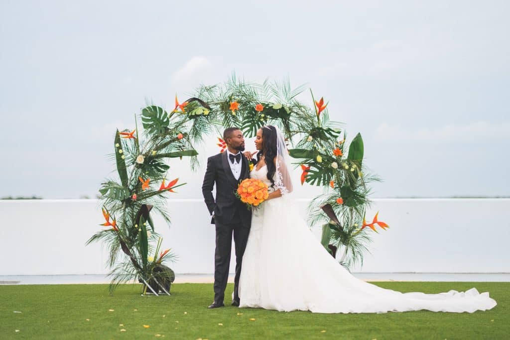 bride and groom standing in front of a floral decorated altar, bride carrying a bouquet of orange flowers, Polk Bros Photo.Video.DJ, Central FL