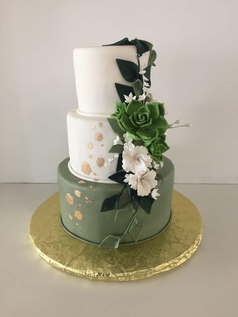 Three layer cake, bottom layer is olive green, top two layers are white with green and white flowers adorned down the right side, gold covered stand, Orlando, FL