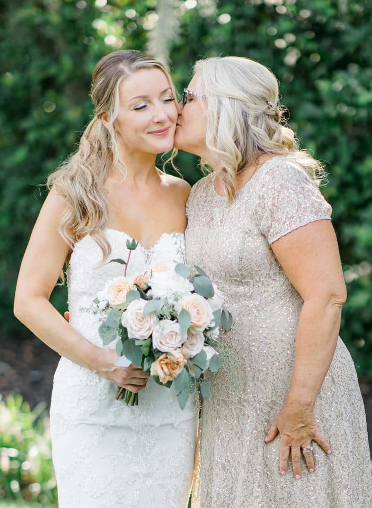 mother of the bride kissing her daughter on the cheek, outdoors, small bouquet of white and pink flowers, Orlando, FL