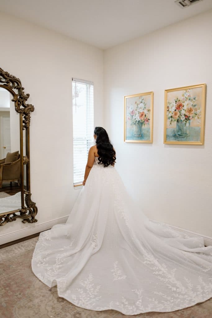 bride wearing her gown, with the train laid out, beautiful lace adorning it, looking out the window, camera taking the photo of her back, Orlando, FL