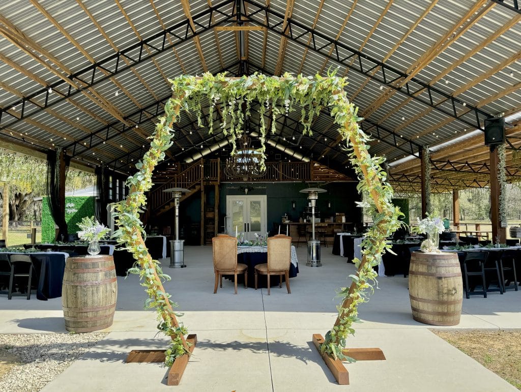 pergola covered in green moss and green flowers and leaves, pavilion above with wooden barrels and the head table in the background, Green Campers Event Venue, Orlando, FL