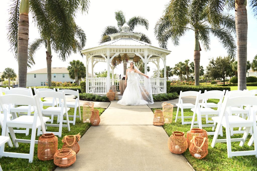 bride posing at the gazebo, white chairs placed in two sections, with a center aisle, baskets with large white candles at the ends of the rows, palm trees, Orlando, FL