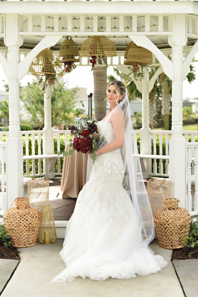 bride posing with her red flower bouquet, facing the camera, at the gazebo, Orlando, FL