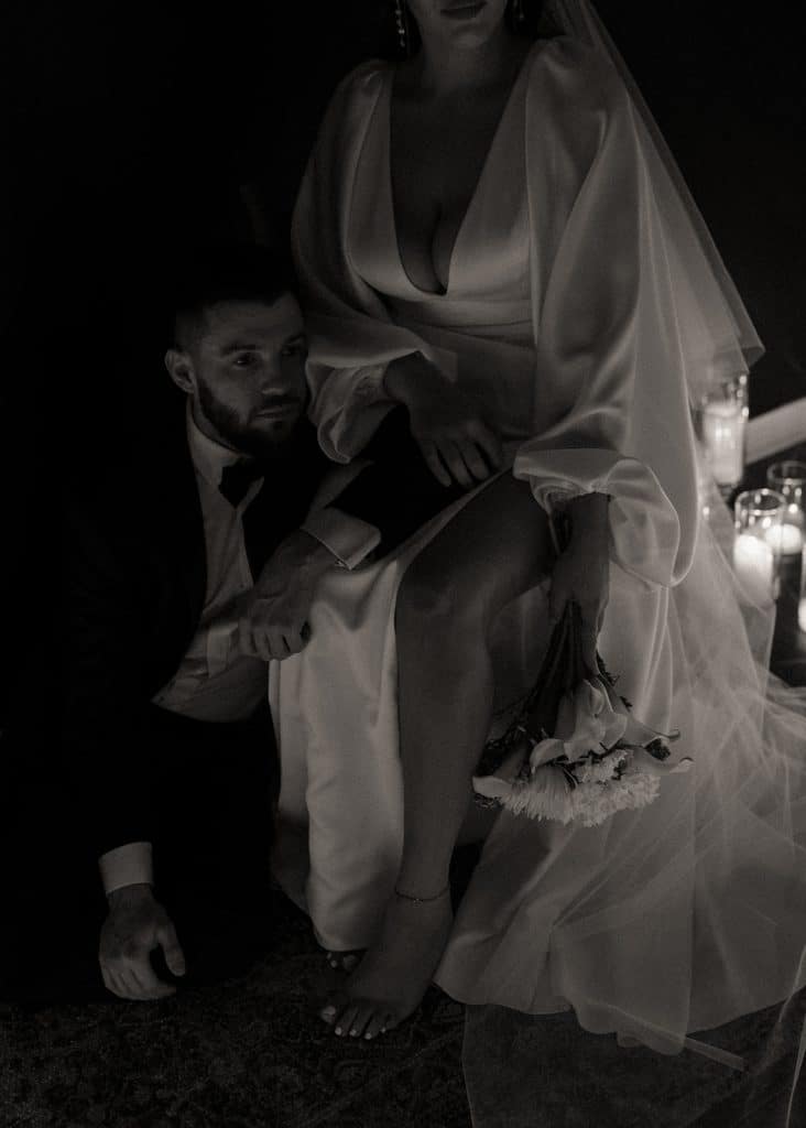 bride sitting in her wedding gown, groom kneeling by her side, lit candles behind them, Orlando, FL