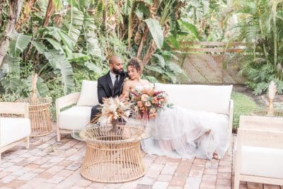 Wedding couple sitting on outdoor patio furniture on their wedding day, surrounded by palm frons, stone patio, Orlando, FL