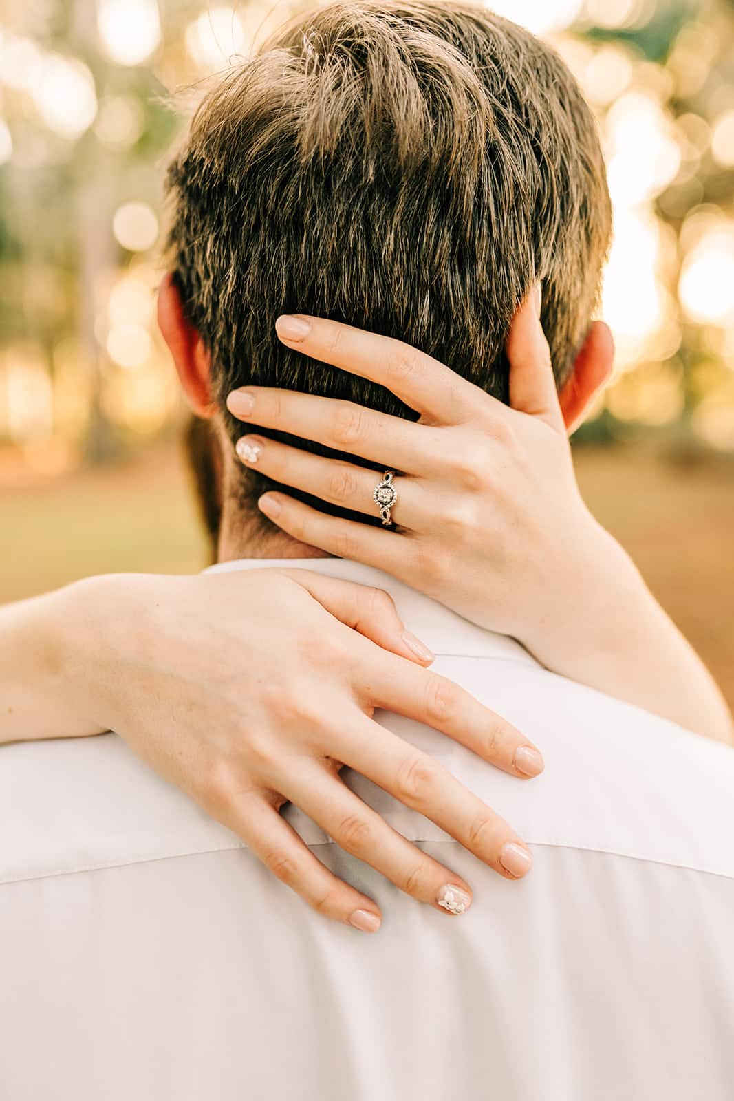 man and woman engagement pictures outside at park close up of woman's hands around neck of man
