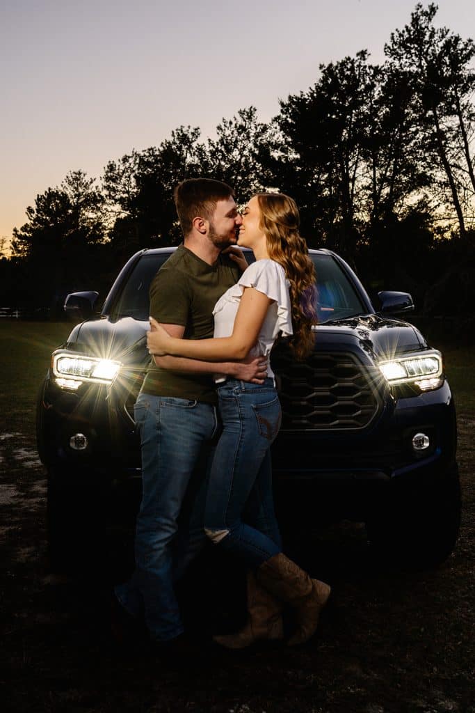 man and woman engagement pictures outside in front of car at dusk