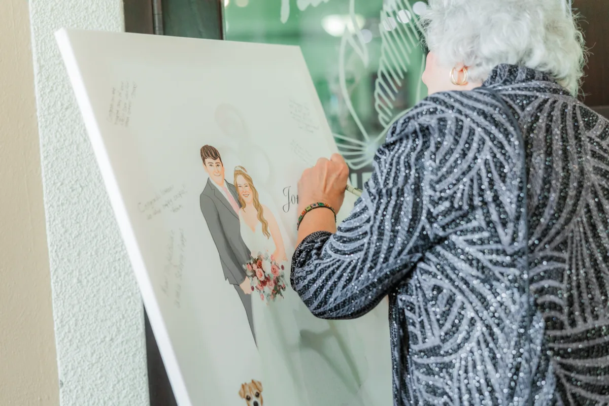 Wedding guest signing a custom illustrated couples portrait guest book canvas at Falcons Fire Golf Club in Kissimmee Florida