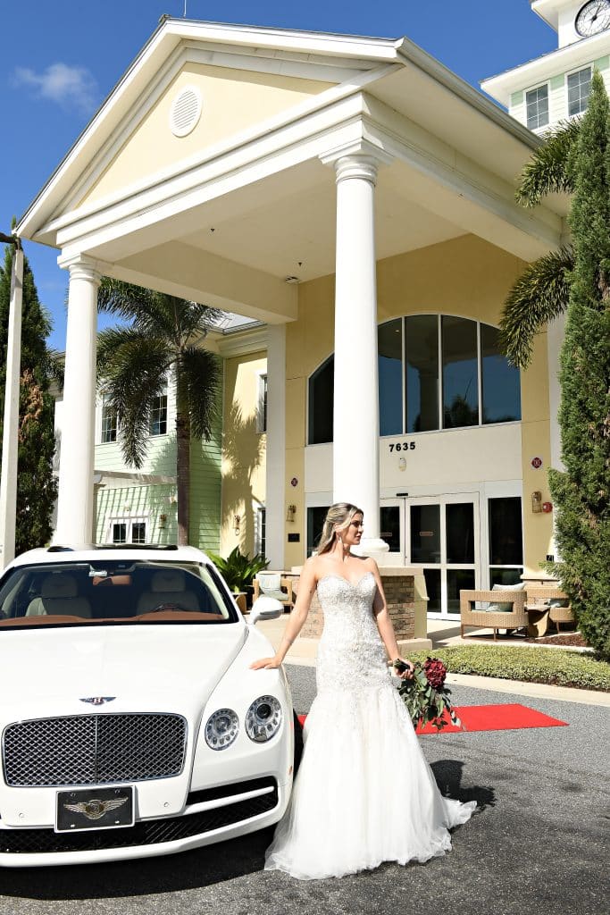 bride standing outside the venue, leaning against a white car, Orlando, FL