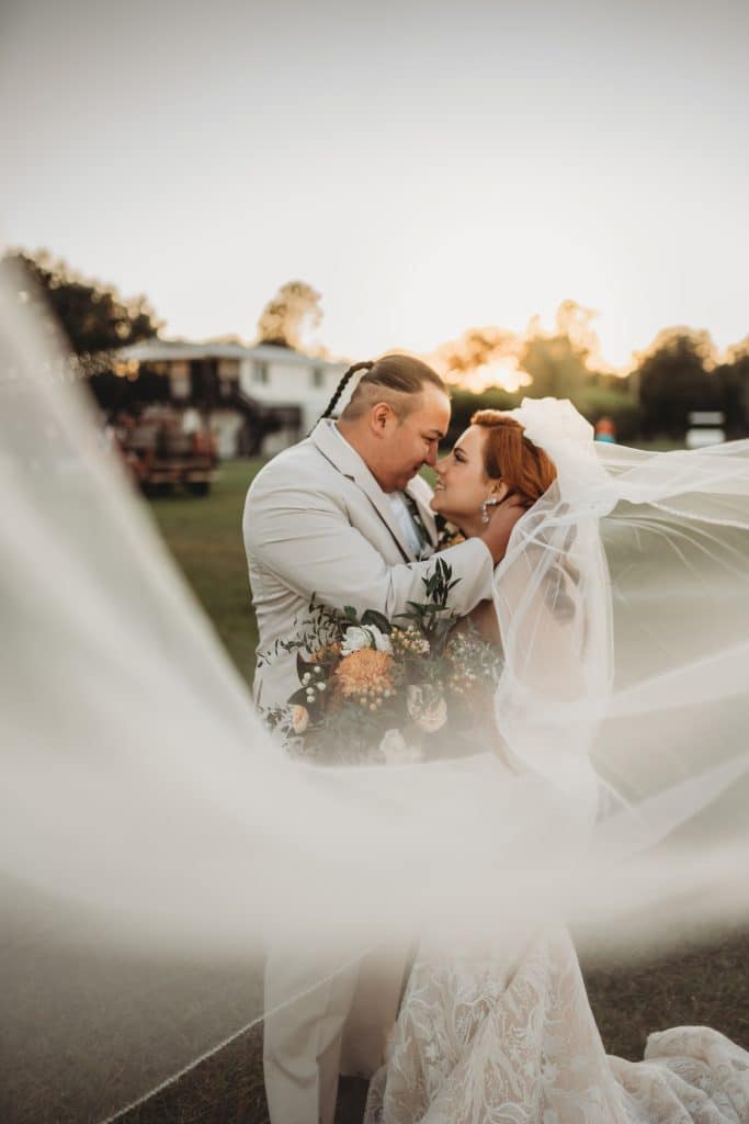 wedding couple kissing, her veil swirling in the wind, almost at sunset, The Enchanting Barn, Orlando, FL