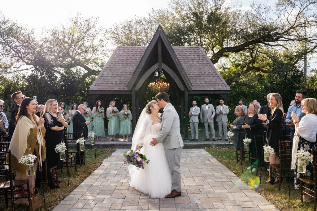 bride and groom kissing after their wedding, guests watching as they embrace, The Enchanting Barn, Orlando, FL